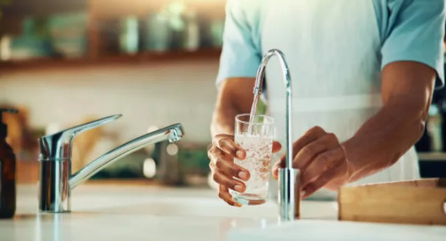Person filling a glass of clean water at a kitchen faucet